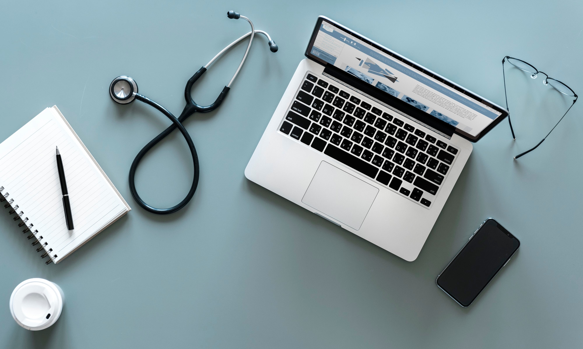 Laptop mit Praxis-Website neben Stethoskop und Smartphone auf einem Schreibtisch